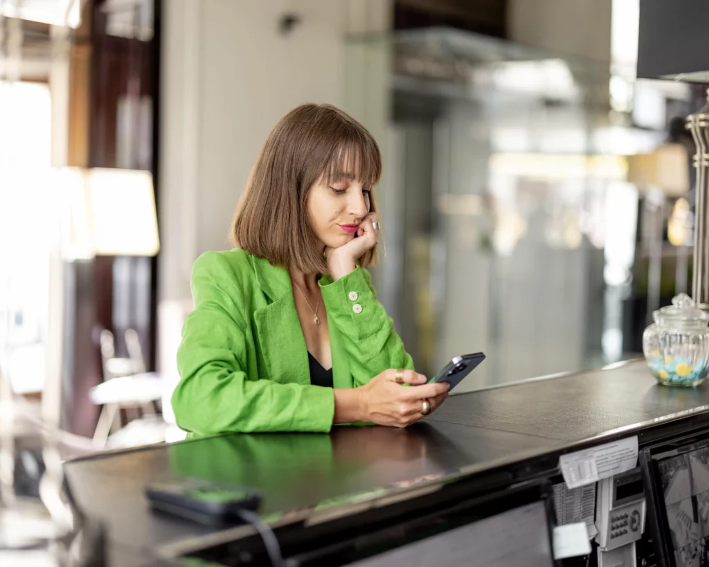 business frau in grünem jacket am tresen sitzend mit handy in der hand in der google my business agentur um google unternehmensprofil optimieren lassen