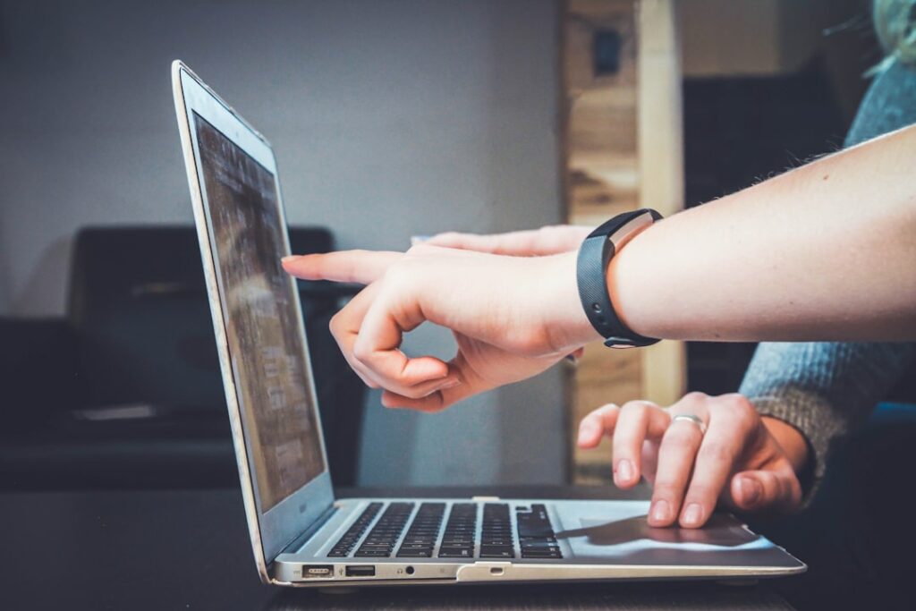 Google Eintrag erstellen: Wie du deine Online-Präsenz optimieren kannst 19 Google My Business optimieren - Es werden zwei Hände gezeigt, die mit einem Laptop interagieren. Eine Hand zeigt auf den Laptop-Bildschirm, während die andere auf der Tastatur ruht. Die Person, die auf den Bildschirm zeigt, trägt ein Armband. Der Hintergrund enthält unscharfe Innenelemente. Local SEO Agentur.