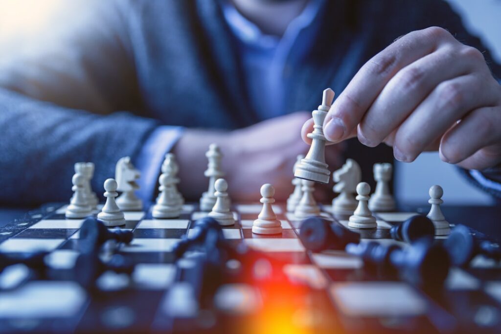 Unternehmensprofil bei Google optimieren 1 google my business optimieren Eine Person bewegt eine weiße Schachfigur auf einem Schachbrett. Das Brett ist mit verschiedenen Schachfiguren bestückt und der Fokus liegt auf der Hand, die die Figur hält. Der Hintergrund ist leicht verschwommen, wodurch das Spiel und die Aktionen des Spielers hervorgehoben werden.